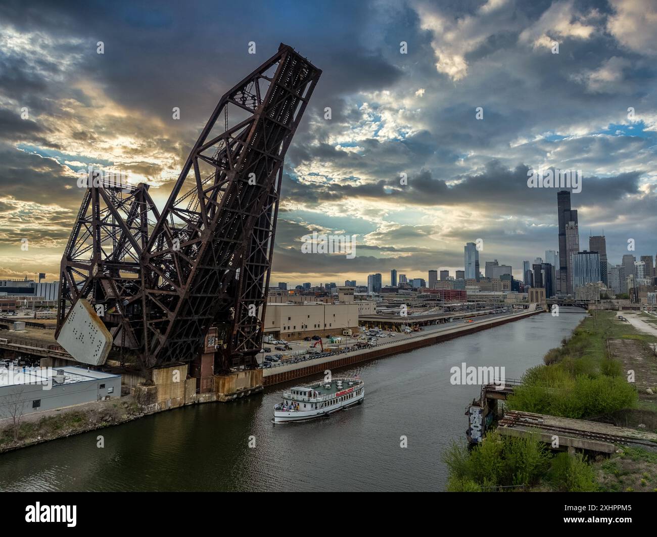 River Boat passe sous le pont Charles Air Line Bridge, pont levis de chemin de fer en acier au-dessus de la rivière Chicago avec le ciel spectaculaire du coucher du soleil Banque D'Images