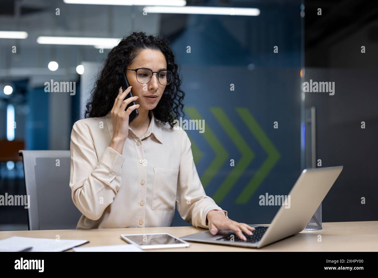 Femme d'affaires multitâche au bureau parlant sur le téléphone et en utilisant un ordinateur portable dans un bureau moderne. Femme professionnelle gérant la communication et les responsabilités professionnelles dans l'environnement de l'entreprise. Banque D'Images