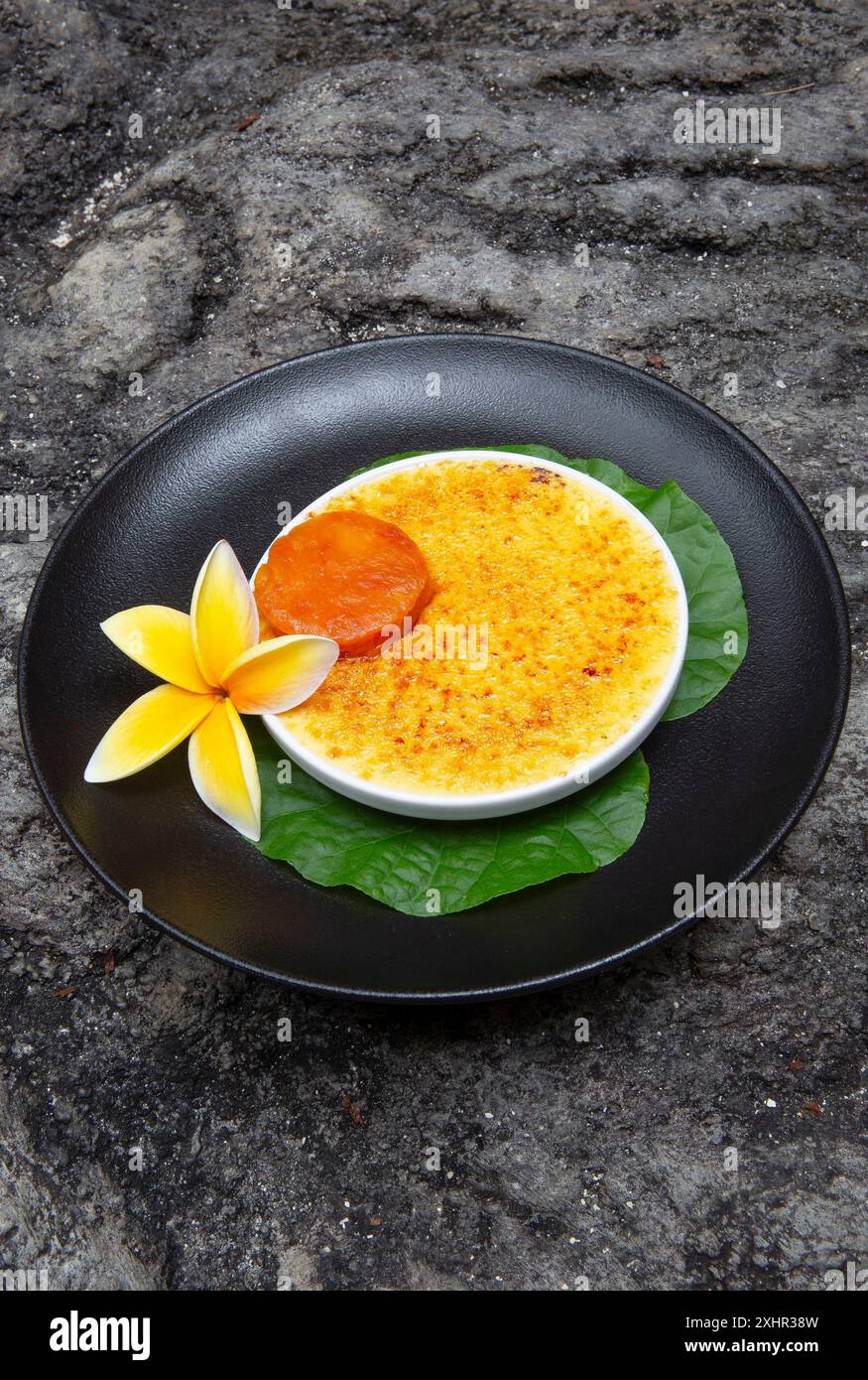 Polynésie française, île de Taha'a, crème brûlée au lait de coco à la vanille tahitienne servie dans une assiette noire sur fond de pierre volcanique, une recette de T. Banque D'Images