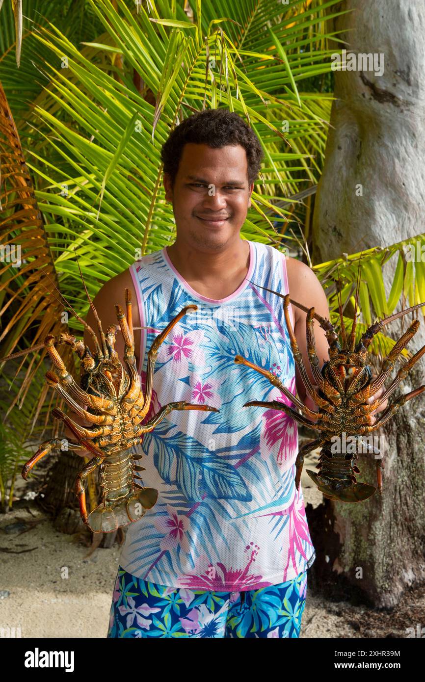 Polynésie française, île de Taha'a, pêcheur tenant de grands homards vivants dans ses mains sur fond de cocotiers Banque D'Images