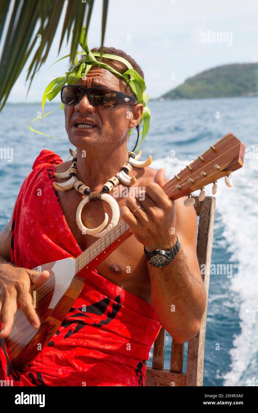 Polynésie française, île de Bora Bora, Rosto, guide polynésien vêtu d'un paréo rouge, couronne végétale sur le crâne et jouant du ukulélé sur son outrig Banque D'Images