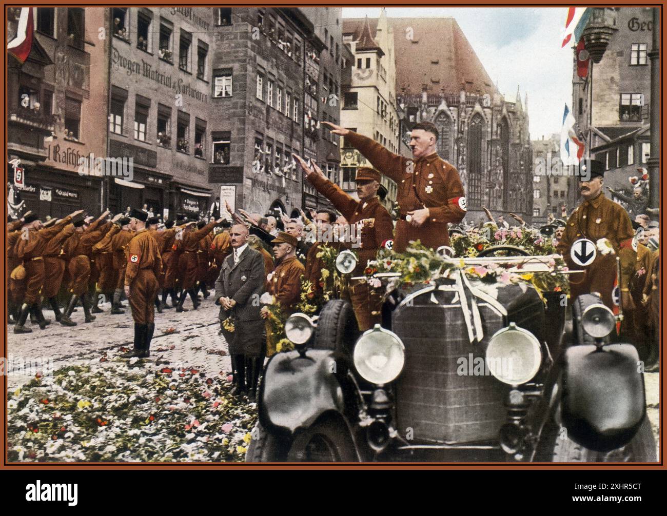 1927 Adolf Hitler debout dans sa voiture Mercedes à toit ouvert au Nuremberg Rally Congress 1927 carte postale en couleurs anciennes, avec des fleurs jetées par des admirateurs, donnant son salut nazi Heil Hitler aux troupes de Sturmabteilung sa défilant et passant dans leurs uniformes de chemise marron avec des brassards Swastika. Julius Streicher un antisémite virulent bien connu et propriétaire de Der Sturmer debout devant Hitler dans un costume sombre. 1927 Banque D'Images