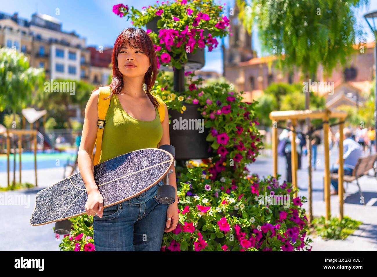 Portrait avec espace de copie d'une jeune femme chinoise portant un skateboard sur une place de ville pleine de fleurs violettes Banque D'Images