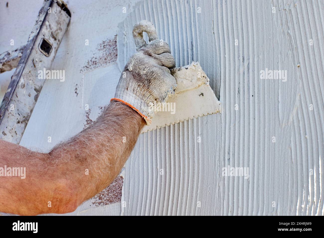 Travaux de finition sur le revêtement de la façade de la maison, le travailleur de la construction applique du mortier adhésif à base de ciment sur les murs et le nivele avec une spatule en acier. Banque D'Images