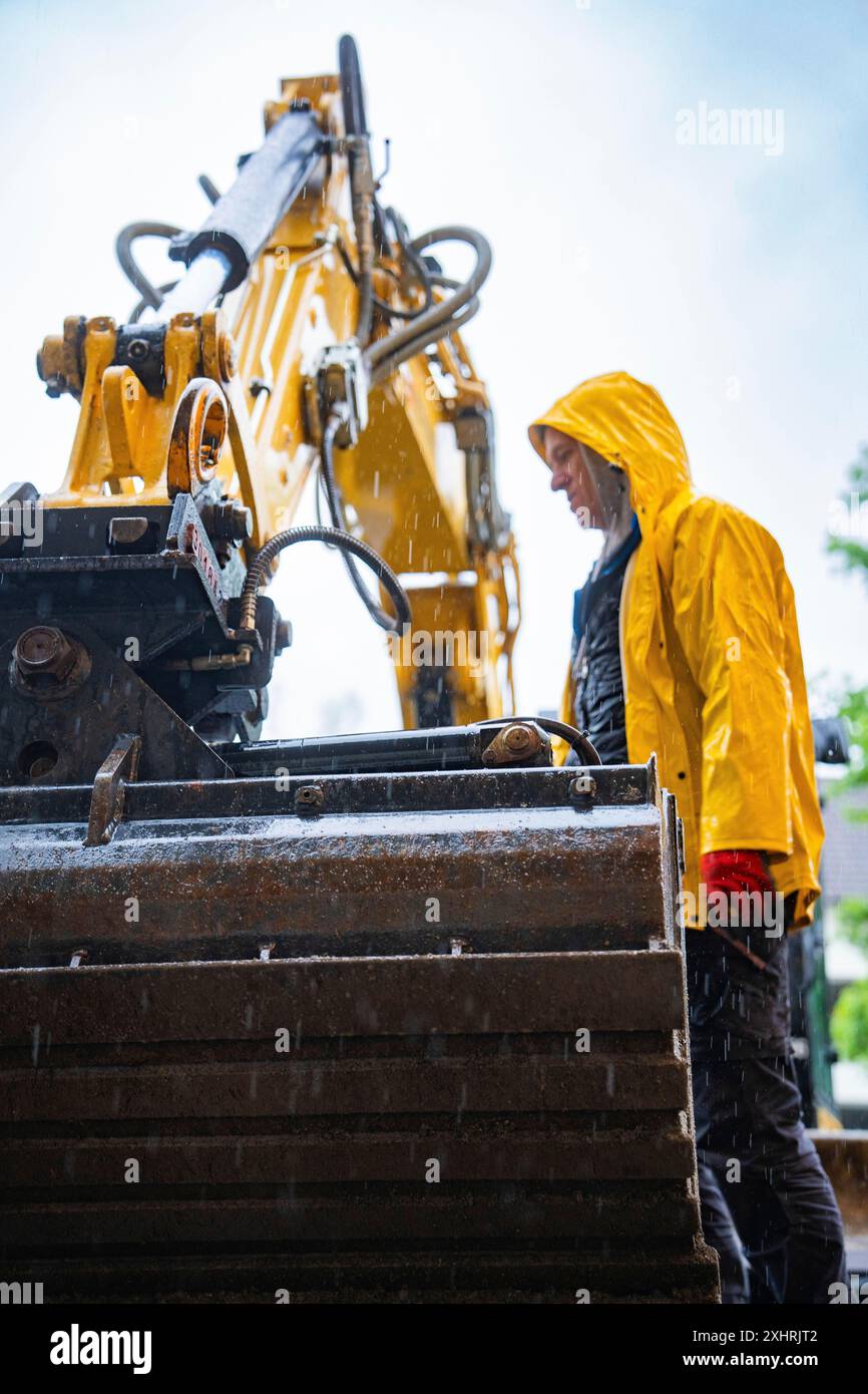 Ouvrier de construction en veste de pluie jaune travaillant avec une grande machine de construction sous la pluie, chantier Hermann Hesse chemin de fer, Calw, Noir Banque D'Images