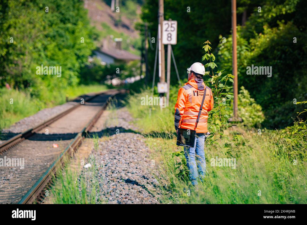 Un travailleur en vêtements de protection et casque se tient à côté des voies ferrées, entouré par la nature et le feuillage vert par temps ensoleillé, levage de pont Banque D'Images