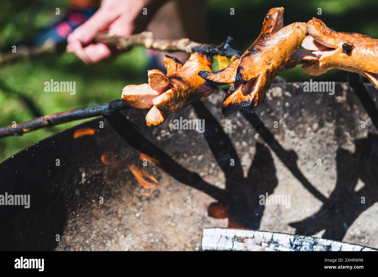 Barbecue en feu. Saucisses chauffant au-dessus du feu de camp en Suisse. Cervelats avec leurs extrémités coupées ouvertes à la manière suisse traditionnelle. Banque D'Images