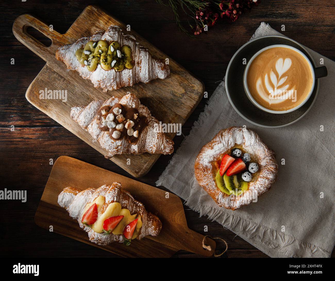 Croissants gastronomiques fraîchement cuits et pâtisserie feuilletée avec baies, confiture, chocolat et pistache. Tasse de cappuccino sur fond en bois foncé. Vue de dessus. Banque D'Images