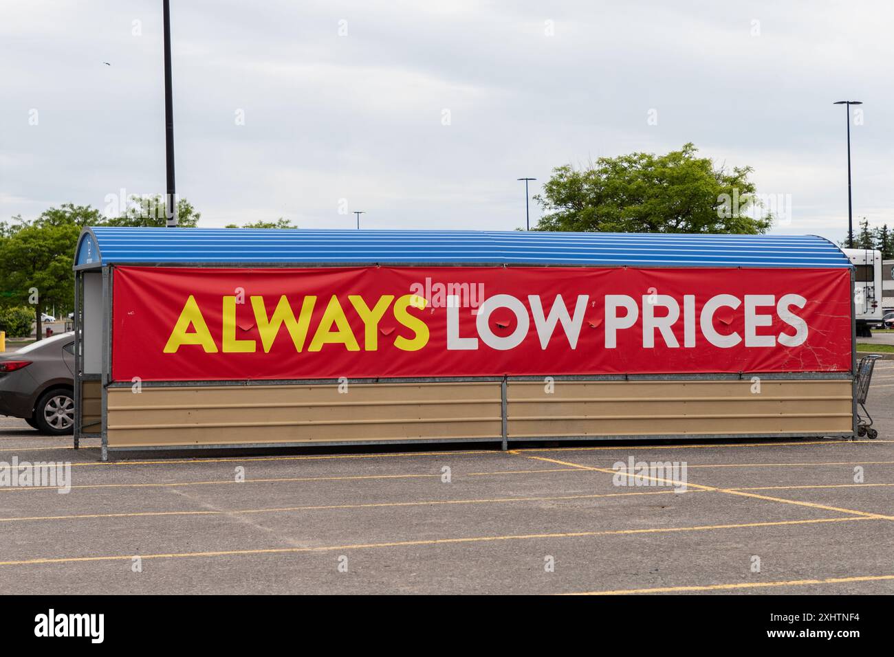 Kanata, Canada - 2 juin 2024 : toujours bas prix affiche une bannière à l'entreposage des chariots au supercentre Walmart. Aire de stationnement du grand magasin. Banque D'Images