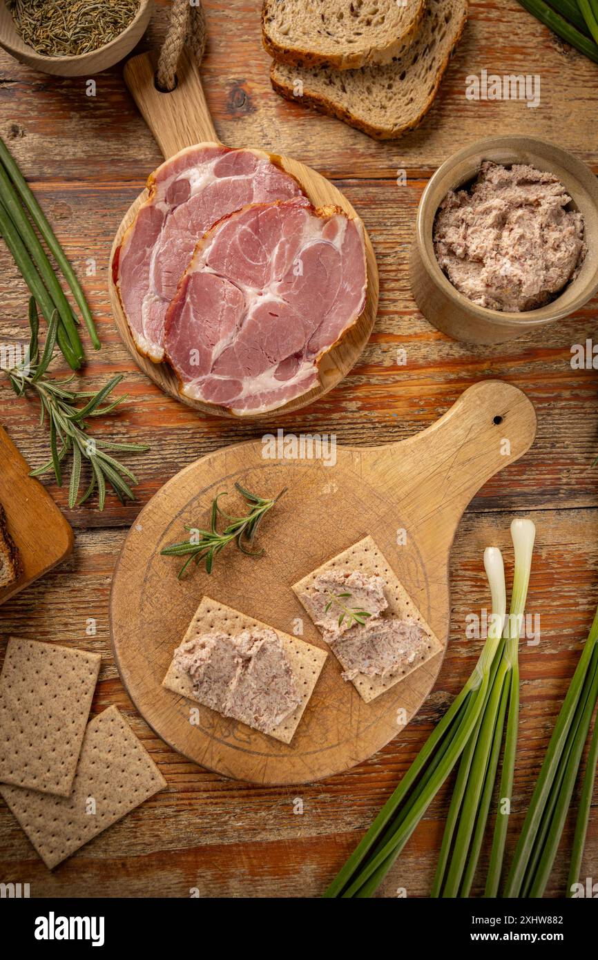 La vue de dessus de la tartinade à la viande est placée sur des craquelins sur une planche de bois avec des oignons verts frais et du romarin Banque D'Images