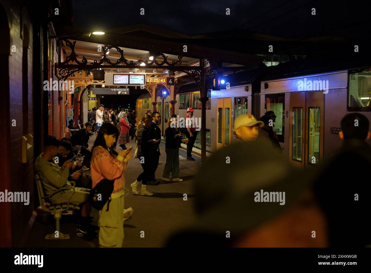 La gare de Sydenham dans le centre-ouest de Sydney la nuit avec des navetteurs debout sur le quai pendant qu'un train tire Banque D'Images