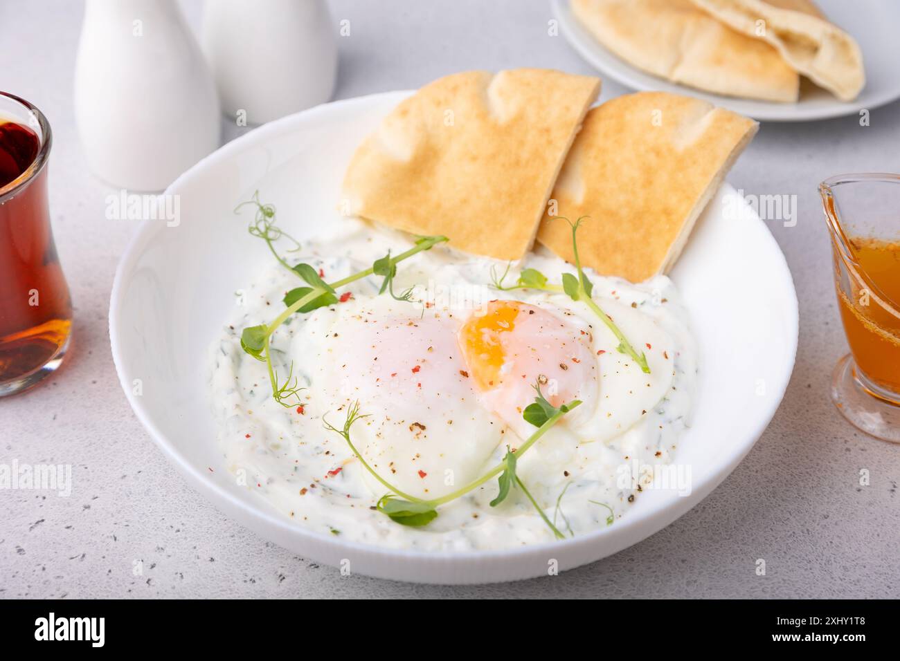 Œufs turcs (chilbir) avec yaourt, beurre parfumé, pousses de pois, pain plat et thé. Petit-déjeuner turc traditionnel avec œufs pochés (avec jaune d'œuf liquide Banque D'Images