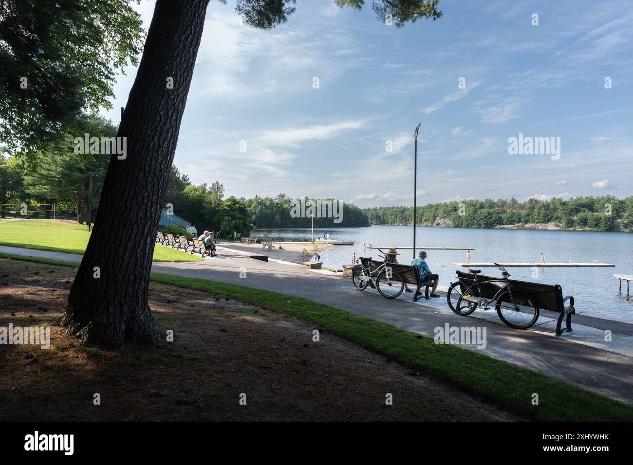 Un parc serein au bord du lac avec des bancs, des vélos et des gens qui apprécient la vue par une journée ensoleillée Banque D'Images