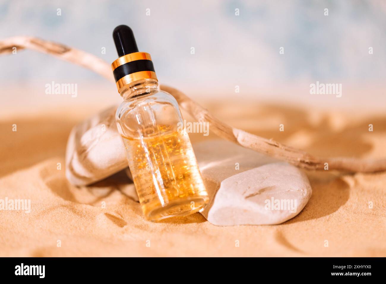 Maquette de bouteille de cosmétiques avec pipette et liquide transparent avec des particules d'or sur sable. Essence de crème solaire dans un tube de verre sur la plage. Hydratant Banque D'Images