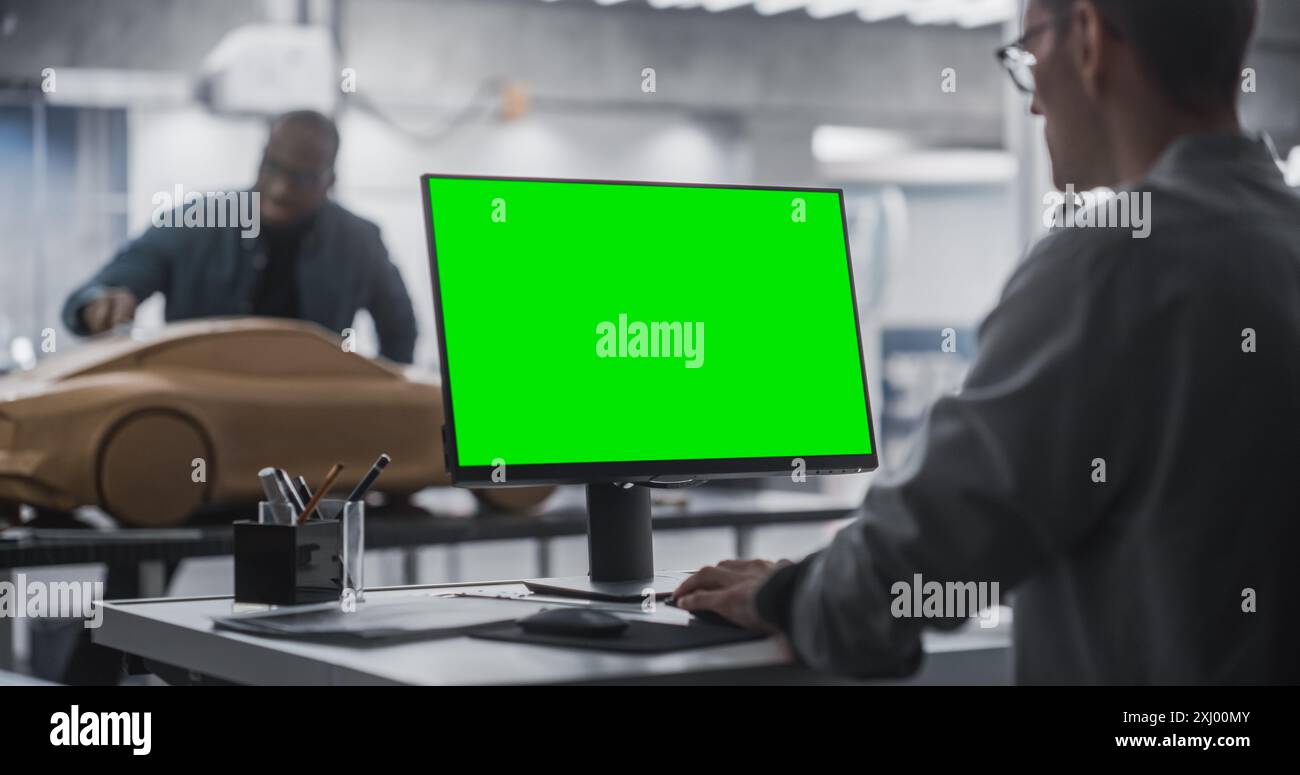 Concepteur automobile travaillant sur un ordinateur de bureau avec écran vert maquette. Artiste numérique créer un véhicule concept dans un studio. Black Male Modeler travaillant sur le modèle d'argile en arrière-plan Banque D'Images