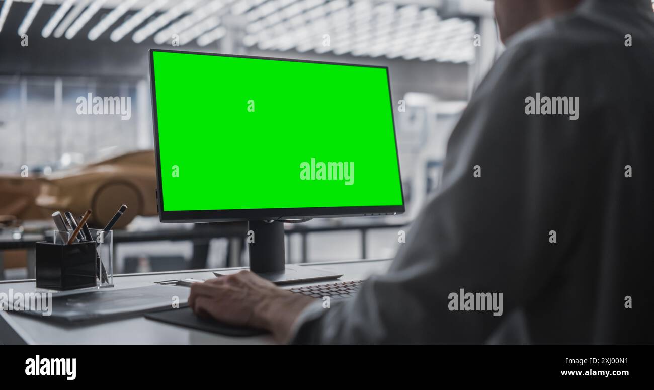 Concepteur automobile travaillant sur un ordinateur de bureau avec écran vert maquette. Artiste numérique créer un véhicule concept dans un studio. Modeleur travaillant avec des équipements technologiques. Banque D'Images