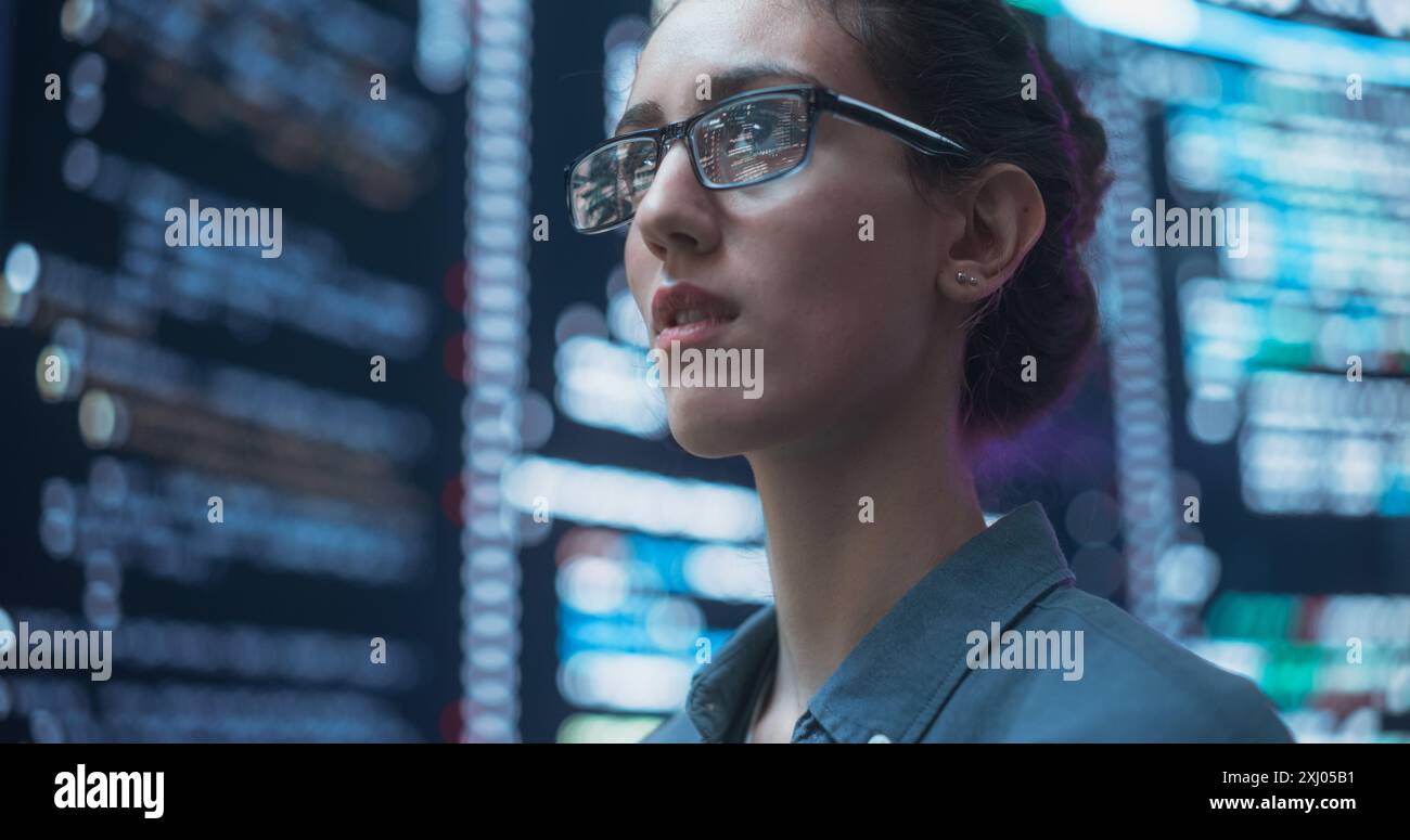 Gros plan Portrait de femme travaillant sur ordinateur, lignes de langage de code reflétant sur ses lunettes de grands écrans d'affichage. Programmeur féminin développant de nouveaux logiciels, codant, gérant la cybersécurité Banque D'Images