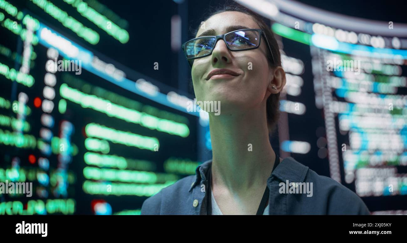 Gros plan Portrait d'une jeune femme avec des lunettes regardant de grands écrans numériques glitching tout en affichant des lignes de code. Pirate professionnel franchissant le système de protection de cybersécurité, changeant le code Banque D'Images