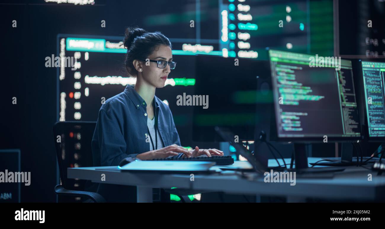 Programmeur féminin travaillant dans la salle de contrôle de surveillance, entouré de grands écrans affichant des lignes de code de langage de programmation. Portrait de femme créant un logiciel. Concept de codage futuriste abstrait Banque D'Images