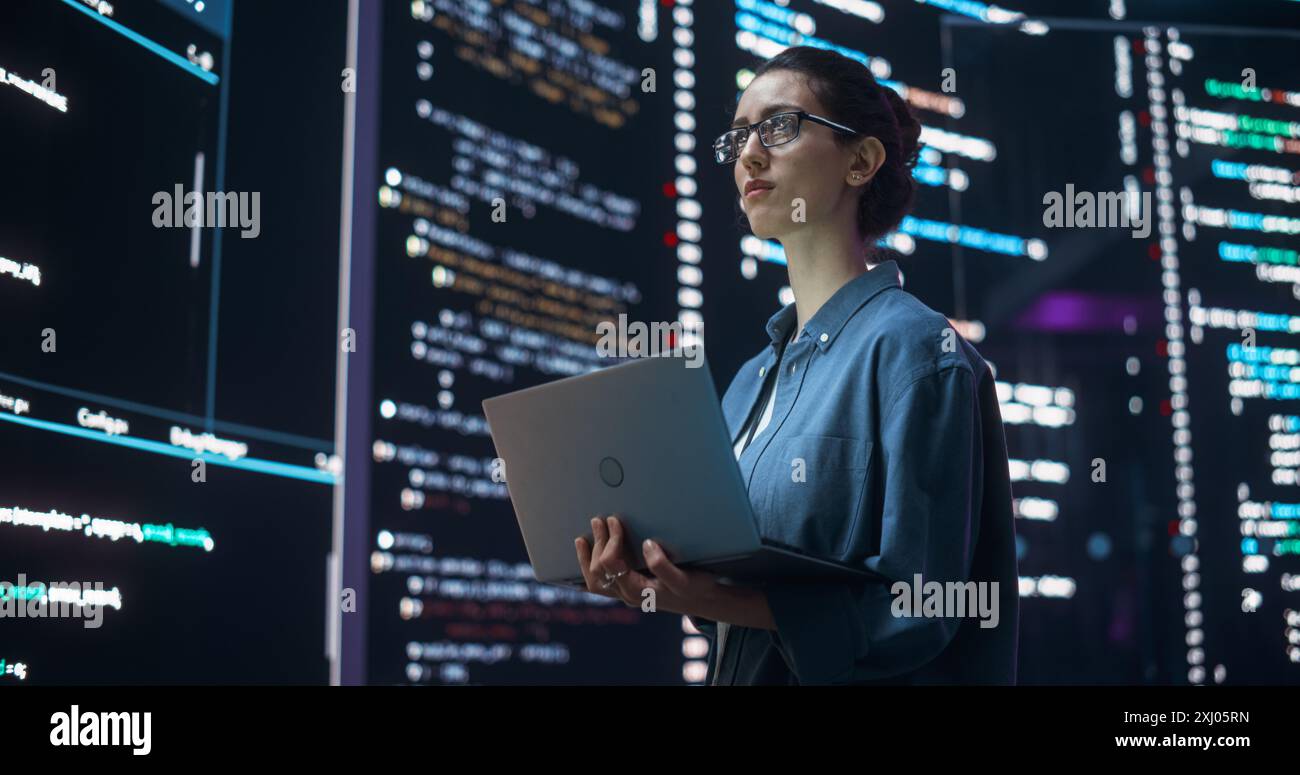 Portrait de femme création d'un logiciel et codage, entouré de grands écrans affichant des lignes de code de langage de programmation. Programmeur féminin travaillant dans une salle de surveillance. Concept futuriste Banque D'Images