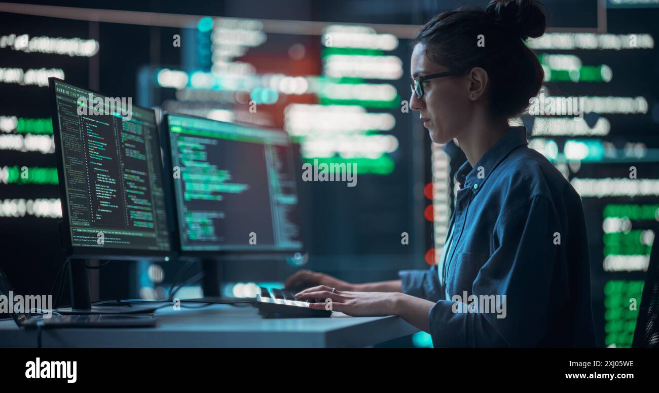 Plan moyen d'une femme travaillant comme développeur, entourée de grands écrans affichant des lignes de code dans la salle de surveillance sombre. Programmeur féminin utilisant un ordinateur de bureau, analyser des données, créer un logiciel d'IA Banque D'Images