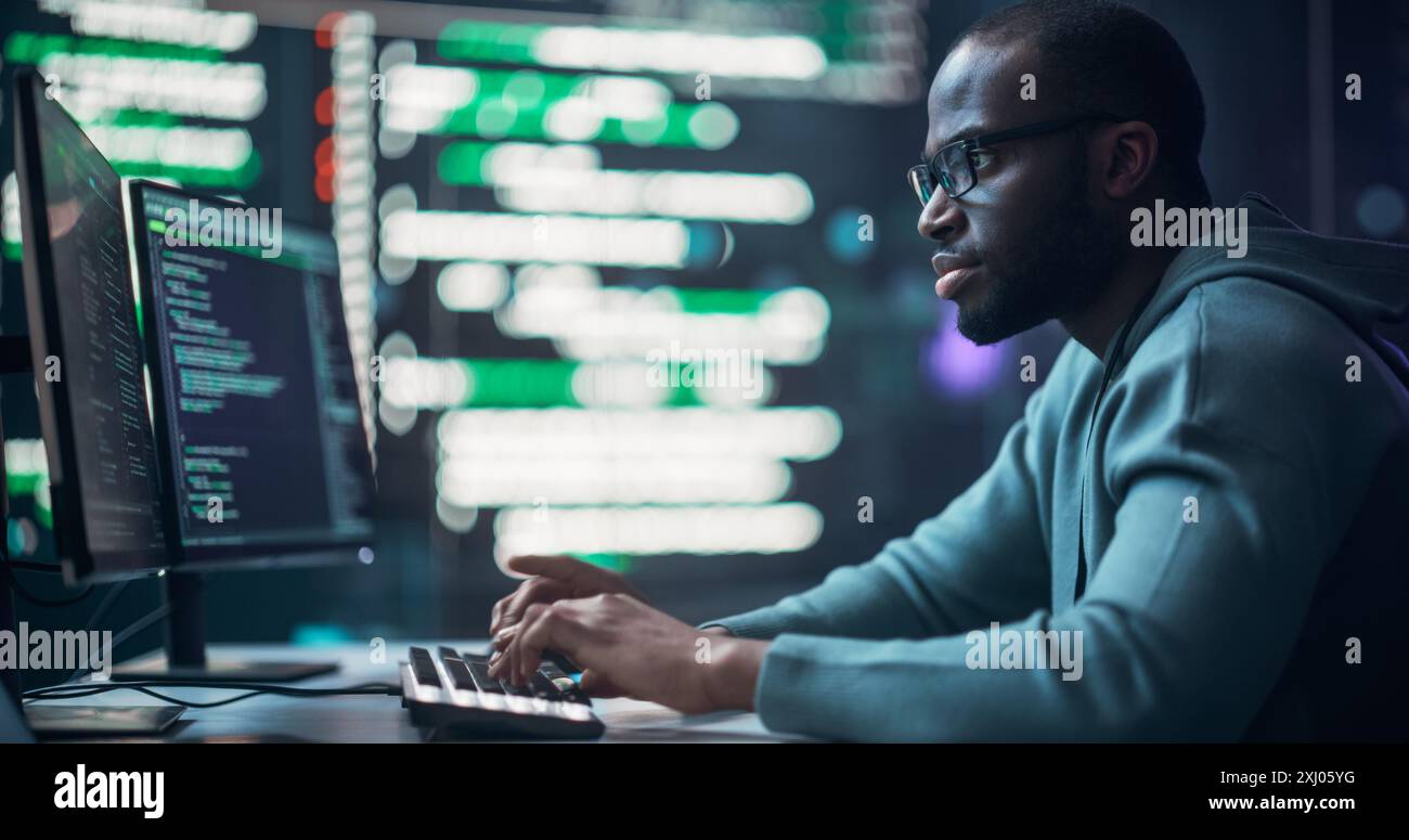 Programmeur masculin noir travaillant dans la salle de surveillance, entouré de grands écrans affichant des lignes de code de langage de programmation. Portrait de l'homme créer un logiciel. Concept de codage futuriste. Banque D'Images