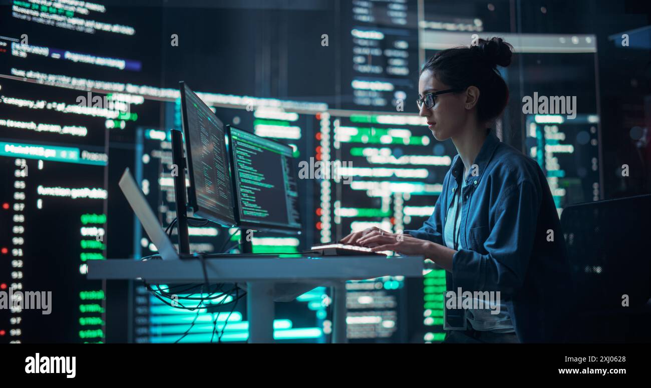 Portrait d'une femme travaillant à l'ordinateur, tapant des lignes de code qui apparaissent sur de grands écrans qui l'entourent dans une salle de surveillance. Programmeur féminin créant un logiciel innovant en utilisant des données et un système ai Banque D'Images