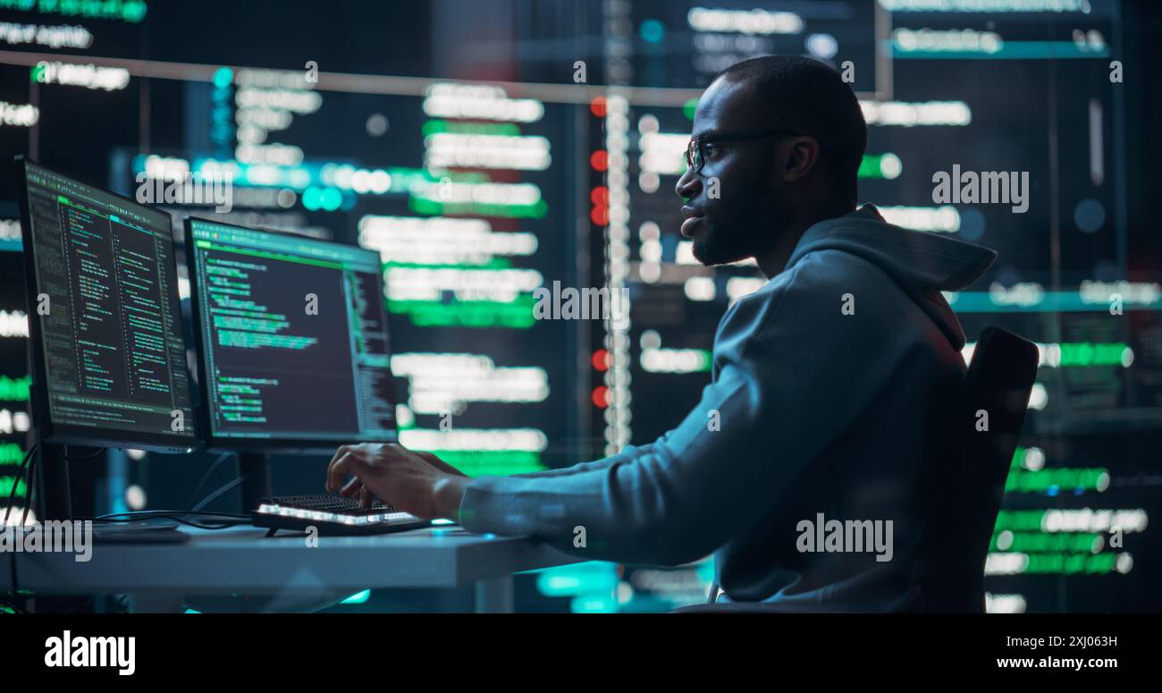 Photo d'un programmeur masculin noir travaillant dans une salle de contrôle de surveillance, entouré de grands écrans affichant des lignes de code de langage de programmation. Portrait d'un homme créant un logiciel et un codage Banque D'Images