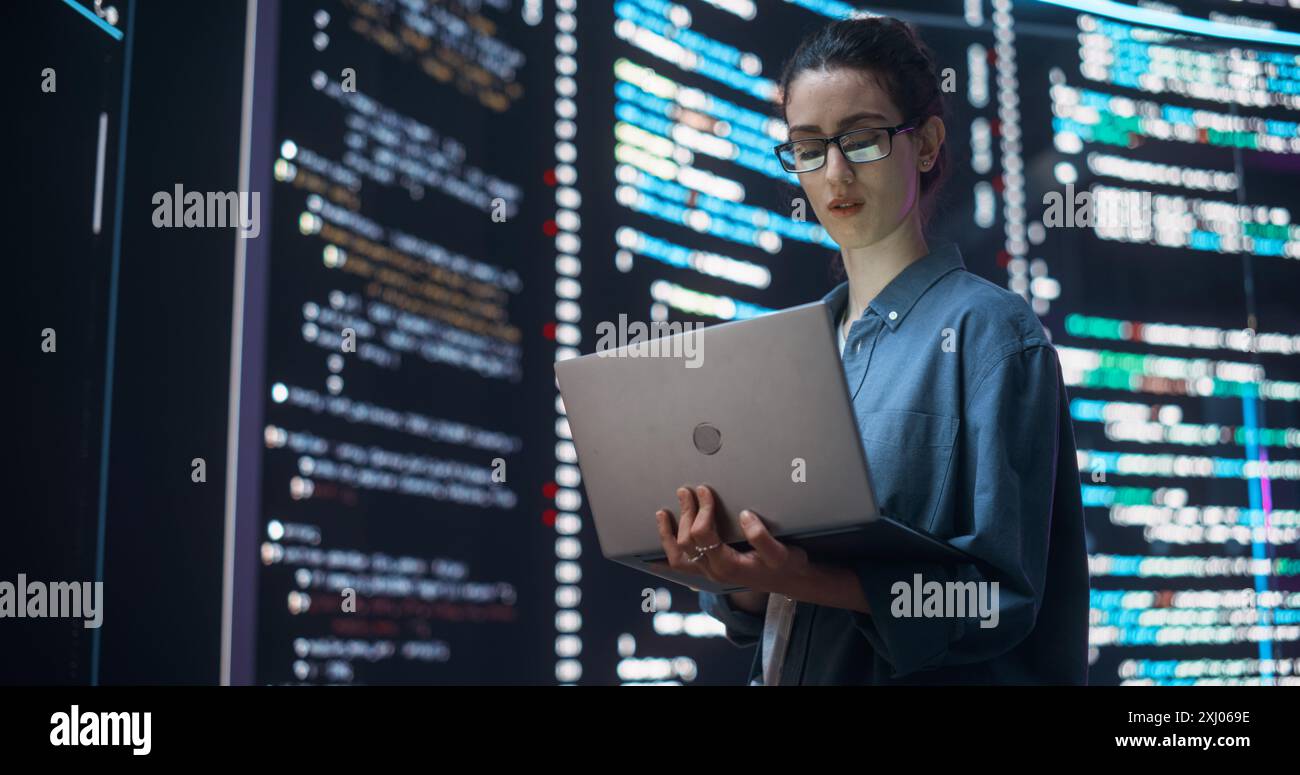Portrait de femme création d'un logiciel et codage, entouré de grands écrans affichant des lignes de code de langage de programmation. Programmeur féminin travaillant dans une salle de contrôle de surveillance. Concept futuriste Banque D'Images