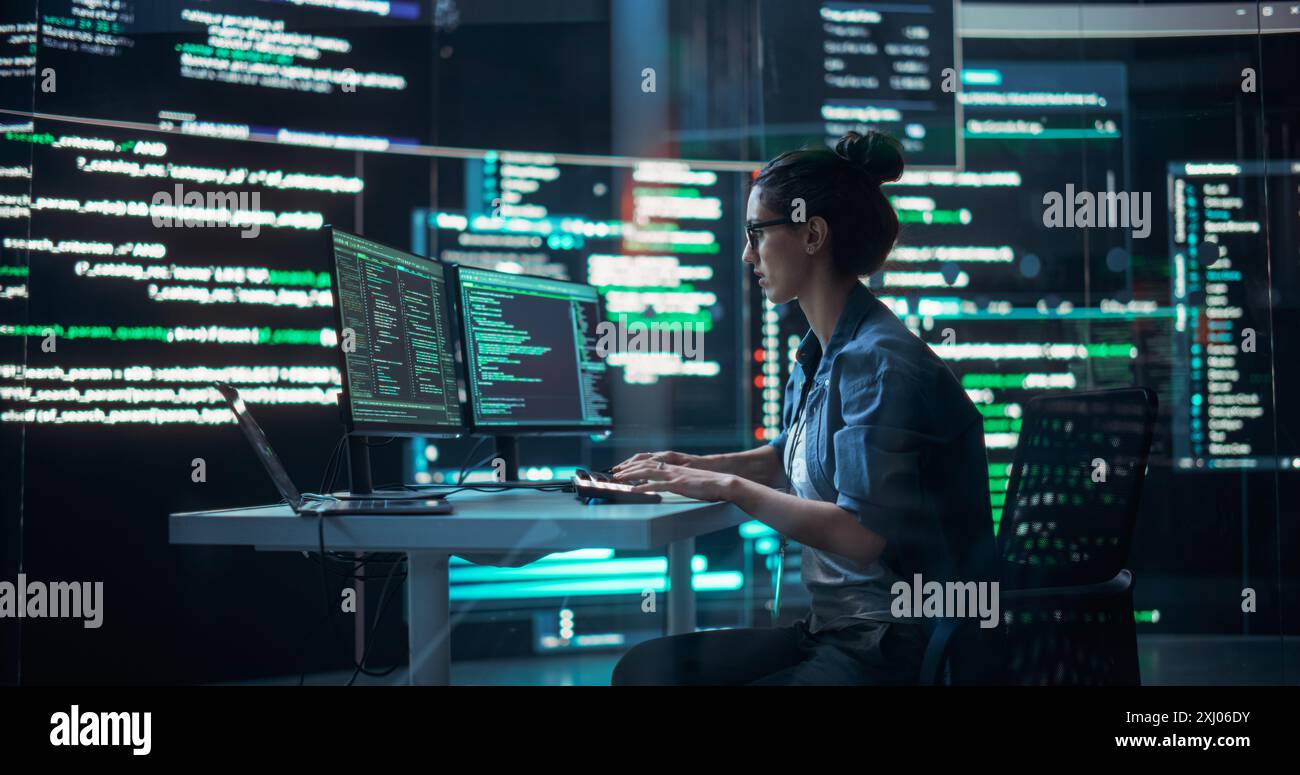 Portrait d'une femme travaillant à l'ordinateur, tapant des lignes de code qui apparaissent sur de grands écrans qui l'entourent dans une salle de surveillance. Programmeur féminin créant un logiciel innovant en utilisant des données et un système ai Banque D'Images