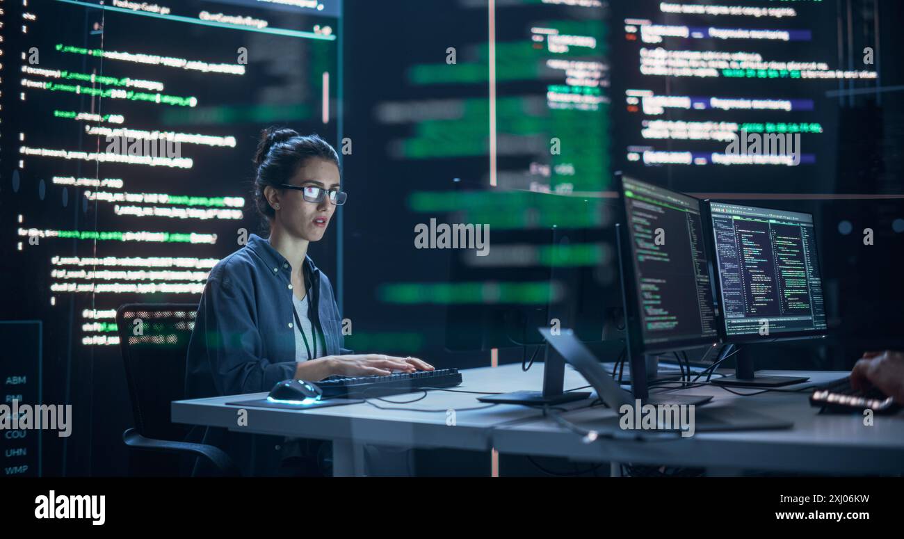 Femme concentrée travaillant comme développeur, entourée de grands écrans affichant des lignes de code dans une salle de surveillance. Programmeur féminin utilisant un ordinateur de bureau, analyser des données, créer un logiciel d'IA Banque D'Images