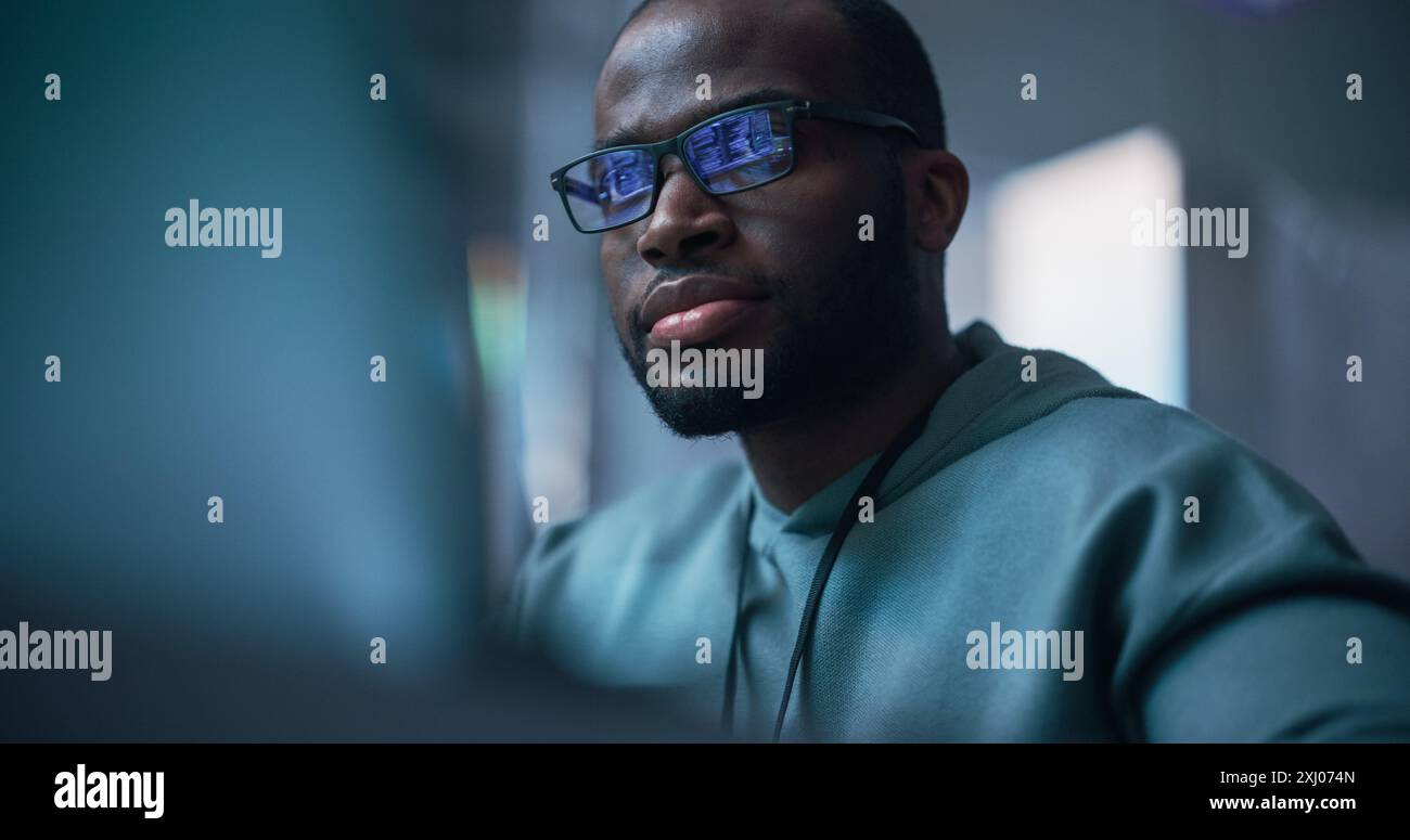Gros plan Portrait d'homme noir travaillant sur ordinateur, lignes de langage de code reflétant sur ses lunettes. Programmeur masculin développant un nouveau logiciel, gérant un projet de défense de cybersécurité. Banque D'Images