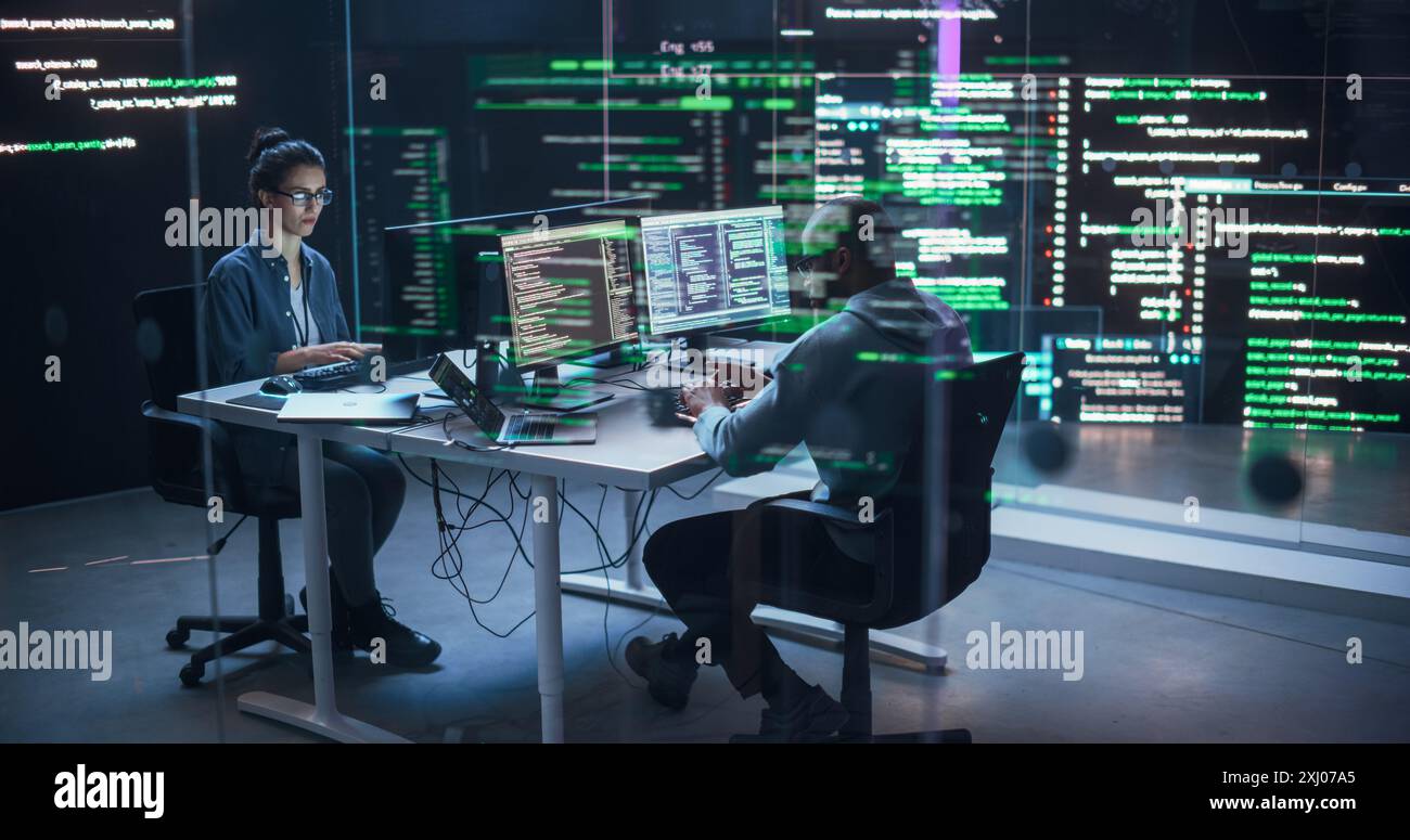 Portrait deux développeurs divers travaillant sur des ordinateurs, tapant des lignes de code qui apparaissent sur les grands écrans qui les entourent. Programmeurs masculins et féminins créant des logiciels innovants, corrigeant des bugs Banque D'Images