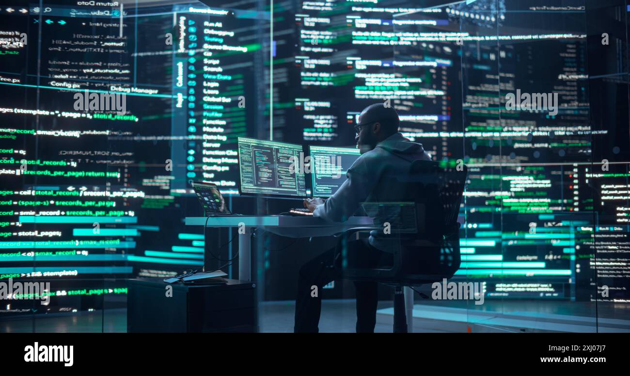 Photo d'un homme travaillant comme développeur, entouré de grands écrans affichant des lignes de code dans une salle de surveillance sombre. Programmeur masculin noir utilisant un ordinateur de bureau, analyser des données, créer un logiciel ai Banque D'Images