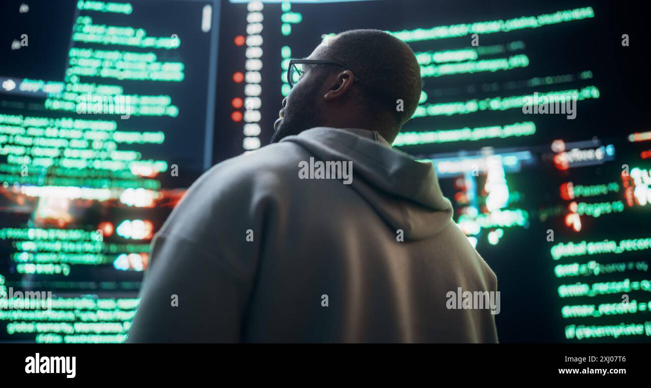 Gros plan vue arrière de jeune homme noir regardant de grands écrans numériques glitching tout en affichant des lignes de code. Pirate professionnel franchissant le système de protection de cybersécurité, changeant le code. Banque D'Images