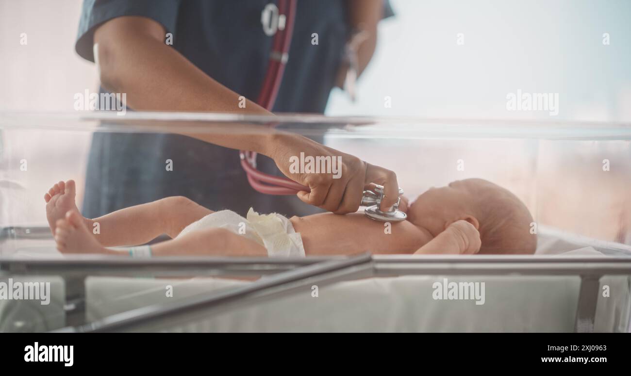 Happy Professional infirmière fournissant des soins 24 heures sur 24 à un bébé prématuré récupéré dans une unité de soins intensifs néonatals. Médecin féminin africain vérifiant sur un enfant, en utilisant stéthoscope dans la clinique de la pépinière Banque D'Images