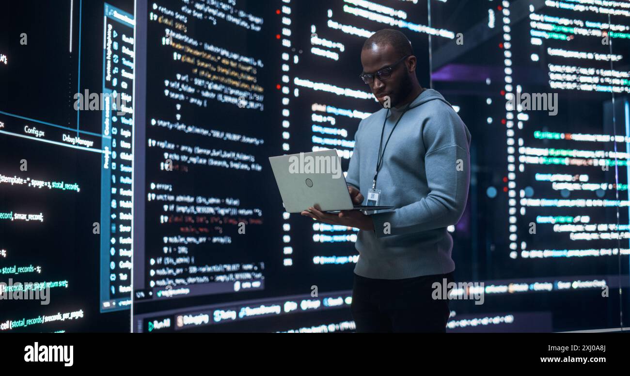 Portrait de jeune homme noir travaillant sur un ordinateur portable, regardant le grand écran numérique affichant des lignes de code back-end. Programmeur professionnel développant un projet de logiciel d'interface Big Data Banque D'Images