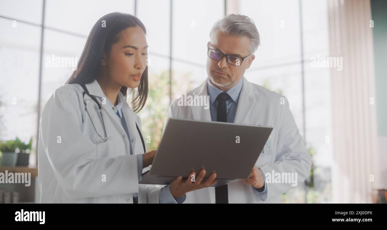 Médecin asiatique professionnel et médecin d'âge moyen ayant une conversation dans un hôpital médical de soins de santé. Collègues utilisant un ordinateur portable, discutant du traitement du patient, des médicaments ou de la thérapie Banque D'Images