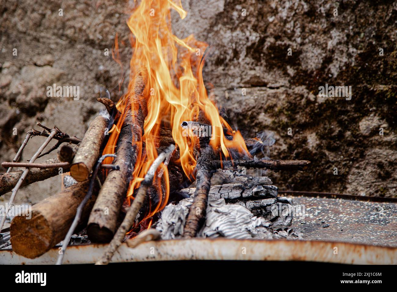 Un petit foyer extérieur brille brillamment avec des bûches et des flammes, placé contre un mur de pierre rustique Banque D'Images