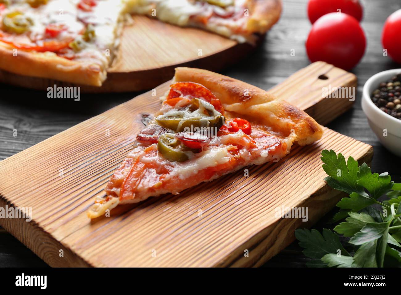 Planche en bois avec une délicieuse pizza Diablo et persil sur la table noire, gros plan Banque D'Images