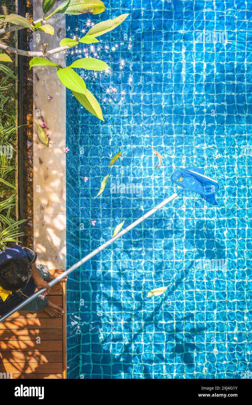 Nettoyage de la piscine des feuilles mortes avec l'équipement de filet skimmer contre les chaises longues de station de soleil à la journée ensoleillée d'été Banque D'Images