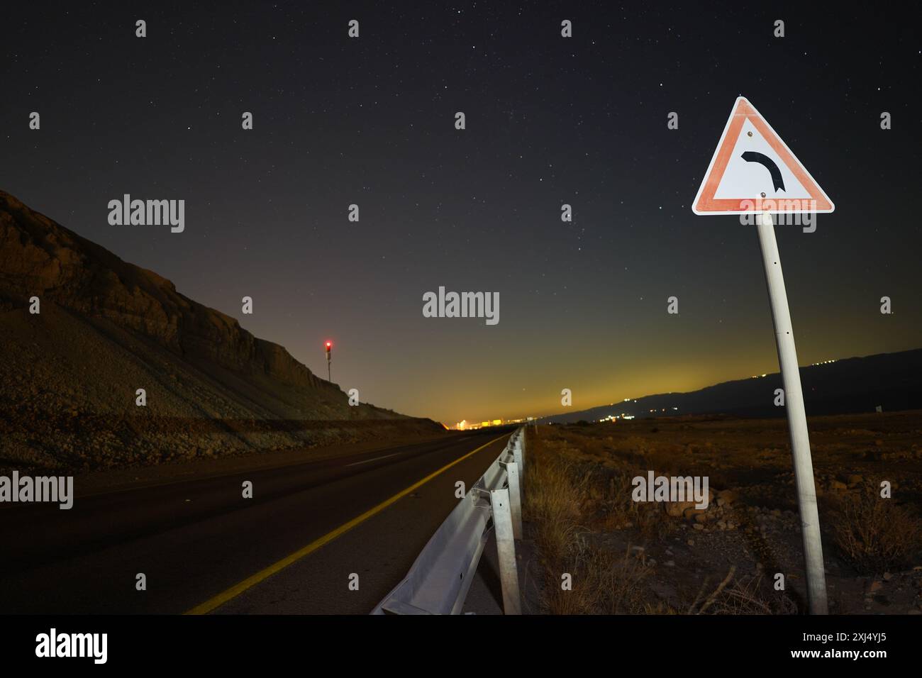 un panneau de signalisation indiquant une courbe à gauche est éclairé sous un ciel étoilé. dans le désert Banque D'Images