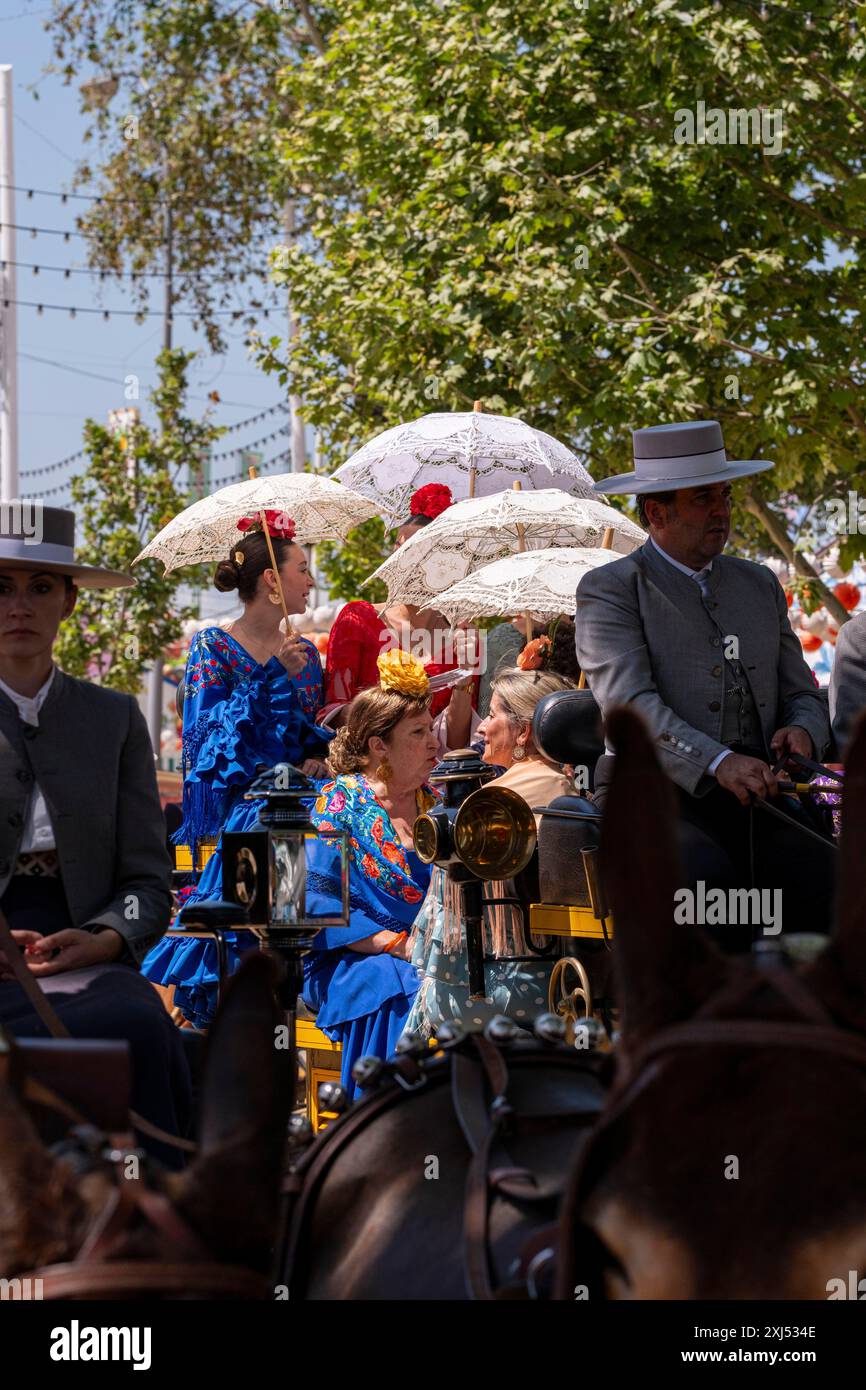 Personnes en tenue traditionnelle chevauchant une calèche sous des parasols dans une rue bordée d'arbres, mai Festivals dans la ville de Séville en Andalousie en Espagne Banque D'Images