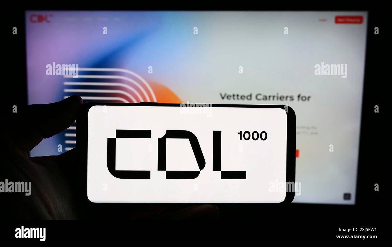 Stuttgart, Allemagne, 02-19-2024 : personne tenant un smartphone avec le logo de la société américaine de services logistiques CDL1000 Inc en face du site. Concentrez-vous sur le téléphone Banque D'Images