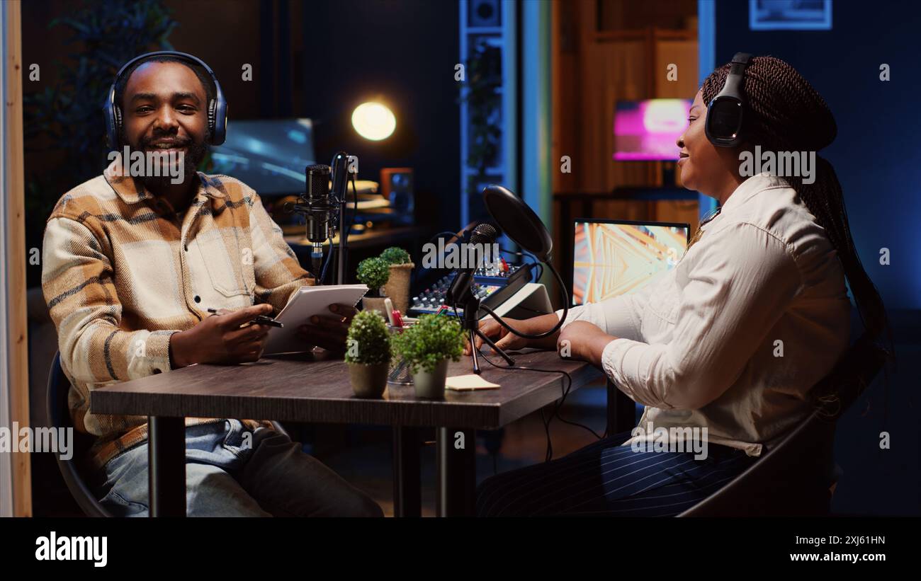 Homme utilisant des microphones high-tech pour assurer une qualité sonore optimale pour l'écoute du public à la maison tout en interrogeant le client. Heureux créateur de contenu utilisant un équipement audio professionnel, présentant la personne interviewée Banque D'Images