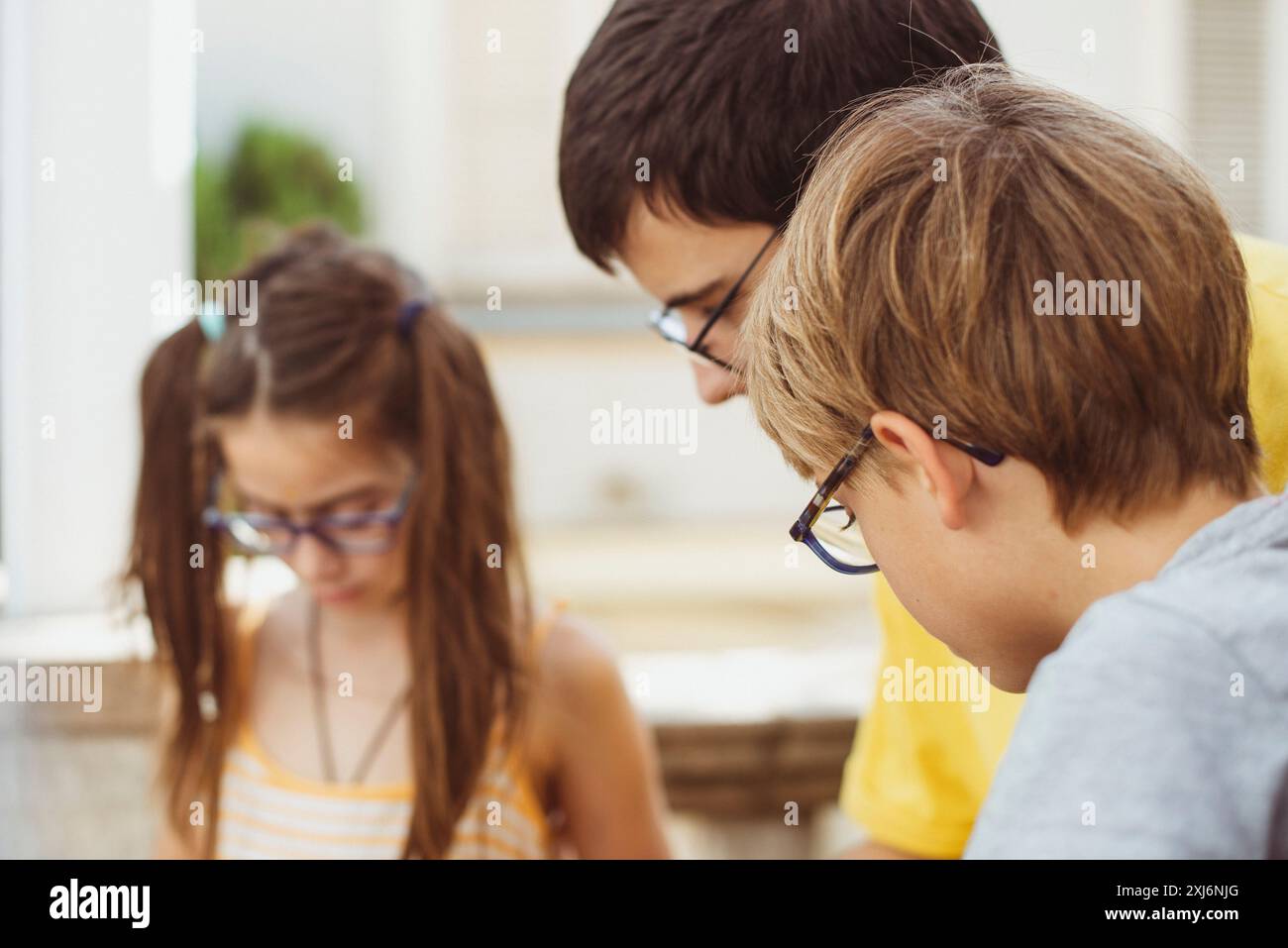 Trois frères et sœurs portant des lunettes debout côte à côte à la maison regardant vers le bas un projet d'étude Banque D'Images