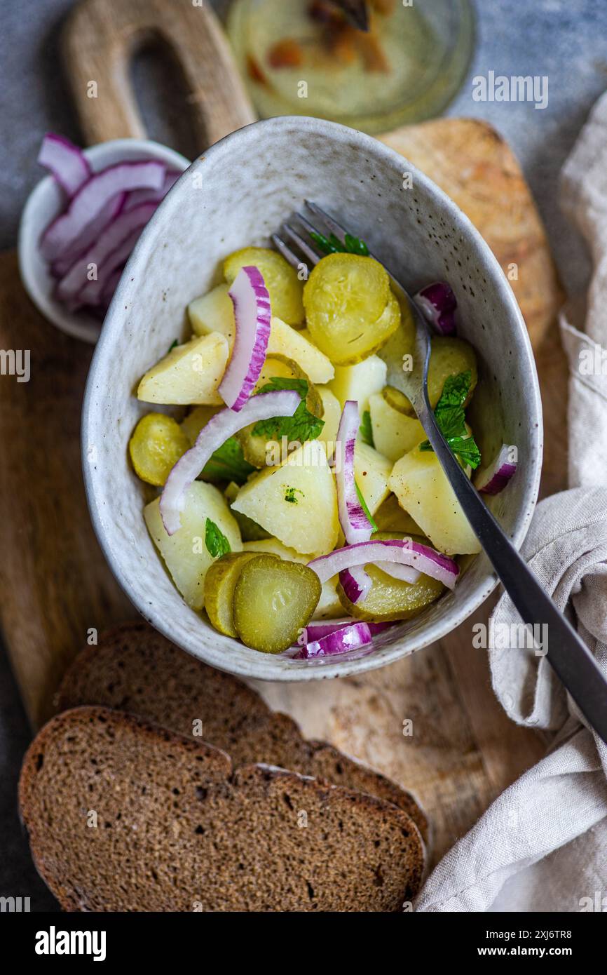 Vue aérienne d'un bol de salade de pommes de terre, oignons rouges et concombre sur une planche à découper avec pain de seigle au levain brun et huile d'olive Banque D'Images