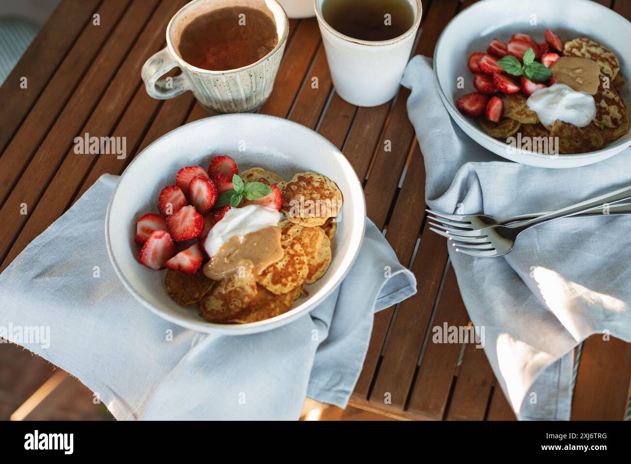 Gros plan de deux petits déjeuners sur une terrasse avec crêpes, fraises, crème, beurre d'arachide et thé Banque D'Images