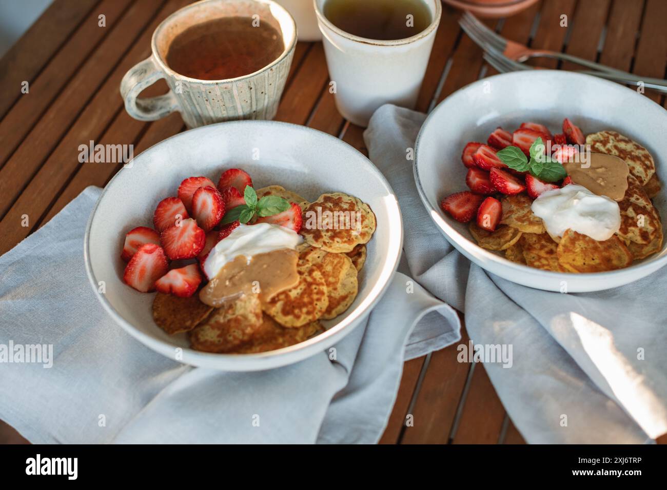 Gros plan de deux petits déjeuners sur une terrasse avec crêpes, fraises, crème, beurre d'arachide et thé Banque D'Images