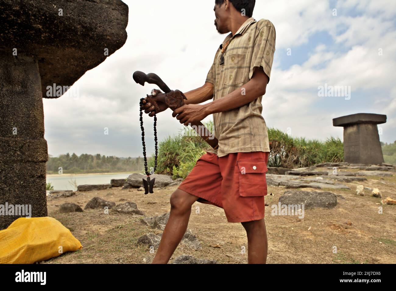 Un villageois vend un collier traditionnel et une machette avec des sculptures traditionnelles sur sa gaine et sa poignée comme souvenirs, alors qu'il se tient près d'un tombeau mégalithique sur la plage de Ratenggaro, un village indigène situé dans le sud-ouest de Sumba, est de Nusa Tenggara, Indonésie. Lors d’une réunion de l’Assemblée générale en décembre 2023, l’Organisation des Nations Unies (ONU) a exprimé ses préoccupations au sujet du détournement et de l’utilisation abusive du patrimoine culturel des peuples autochtones. L’ONU réaffirme que les peuples autochtones ont le droit de maintenir, contrôler, protéger et développer leur patrimoine culturel, leurs savoirs traditionnels et... Banque D'Images